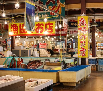 鳥取港海鮮市場かろいち 市場 店内 日本海の豊かな海の幸が水揚げされる賀露(かろ)港のすぐ隣。市場内には12の店舗が並び、水揚げされた新鮮な魚介類をはじめ、鳥取ならではの食品、お土産など多彩にそろいます。新鮮な海鮮料理がリーズナブルに楽しめる市場料理の店やとうふちくわの専門店など飲食店も充実。地元産の野菜や果物などが販売されている地場産プラザ『わったいな』も隣接し、鳥取の食の台所とよばれています。鳥取県鳥取市賀露町西