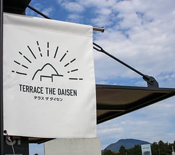 テラス ザ ダイセン 外観『大山(だいせん)ハム』の新工場「大山工場」の直売所&テイクアウトショップ。雄大な大山を仰ぎ見る絶好のロケーションにあり、『大山ハム』こだわりの熟成シリーズをはじめとするハム・ソーセージを種類も豊富に提供。テイクアウトで、できたてのジューシーなホットドッグや焼きソーセージ、スイーツやドリンクなどが味わえます。鳥取県西伯郡伯耆町須村